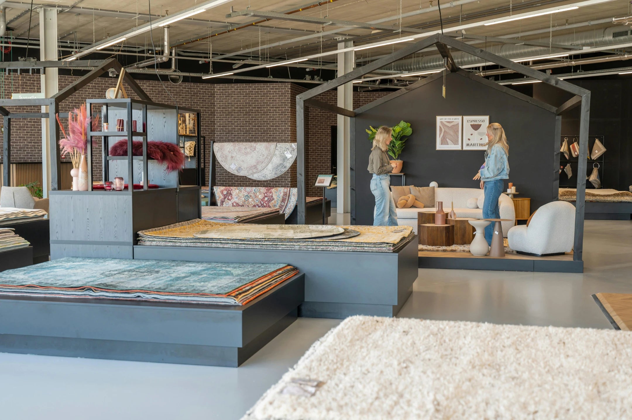 Two visitors talking in a styled living setting inside the Volero Amsterdam showroom, surrounded by stacked rugs on display platforms